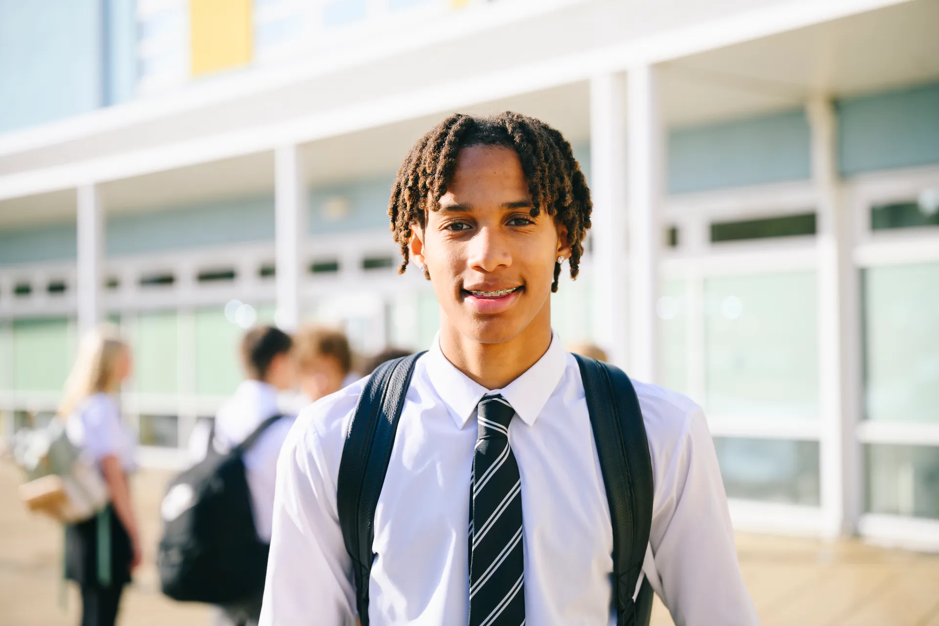 Confident Vaughan College student with braided hair smiling outside school in uniform with striped tie