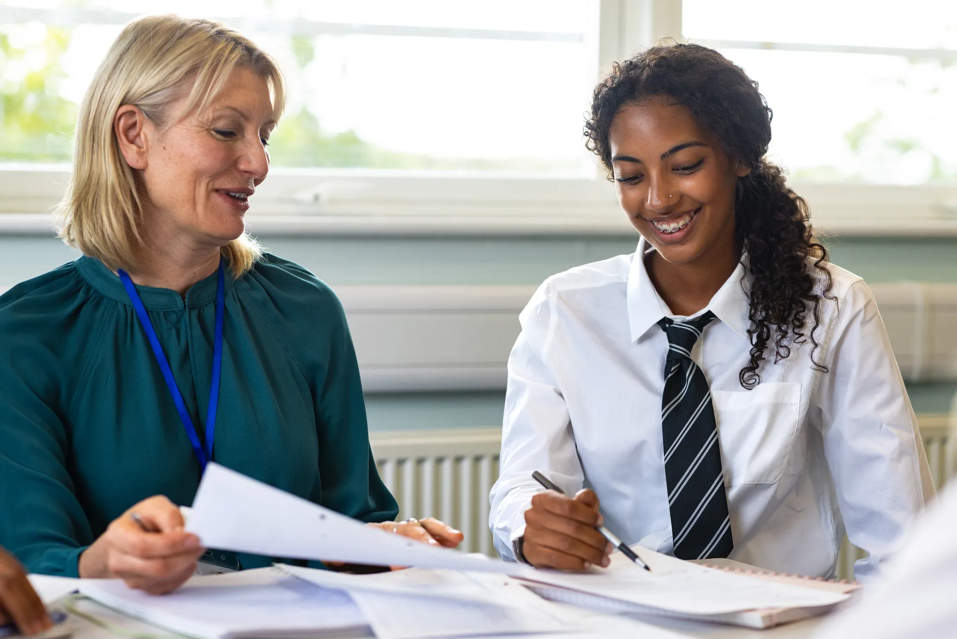 A teacher and Vaughan College student in uniform reviewing work together at a sunlit desk