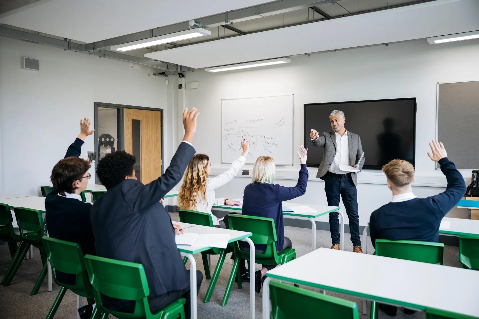 Vaughan College students raising their hands during a class led by a teacher at the front