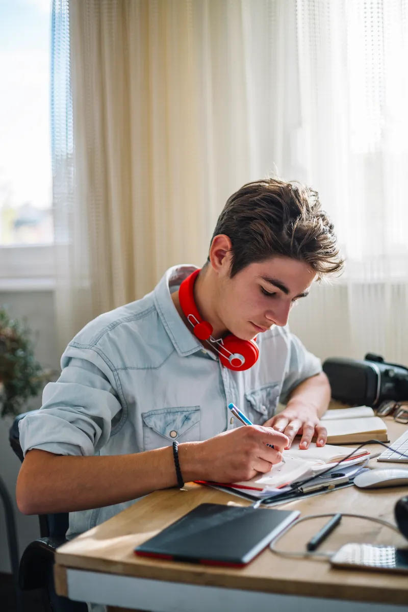 A student writing in a notebook by a sunlit classroom window