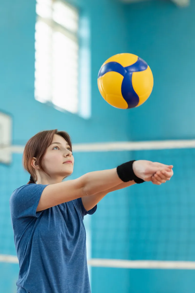 A student bumping a volleyball in the gymnasium