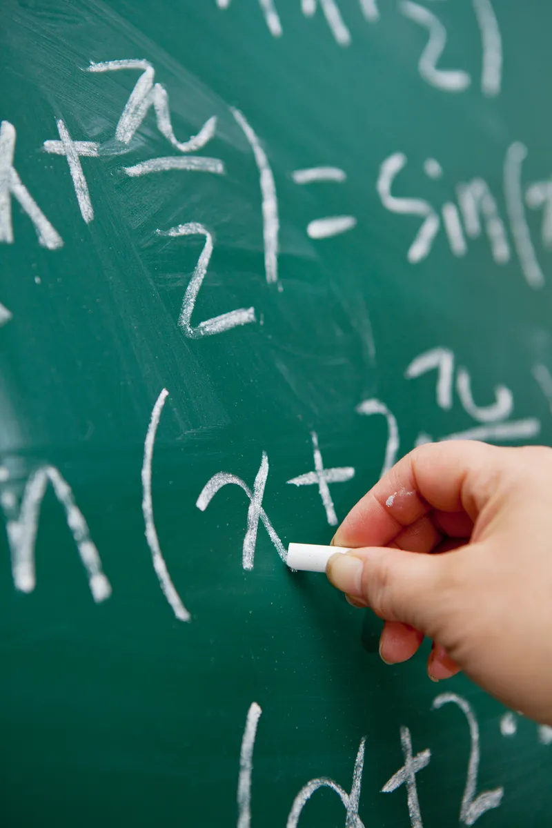 A hand working through algebra on a chalkboard