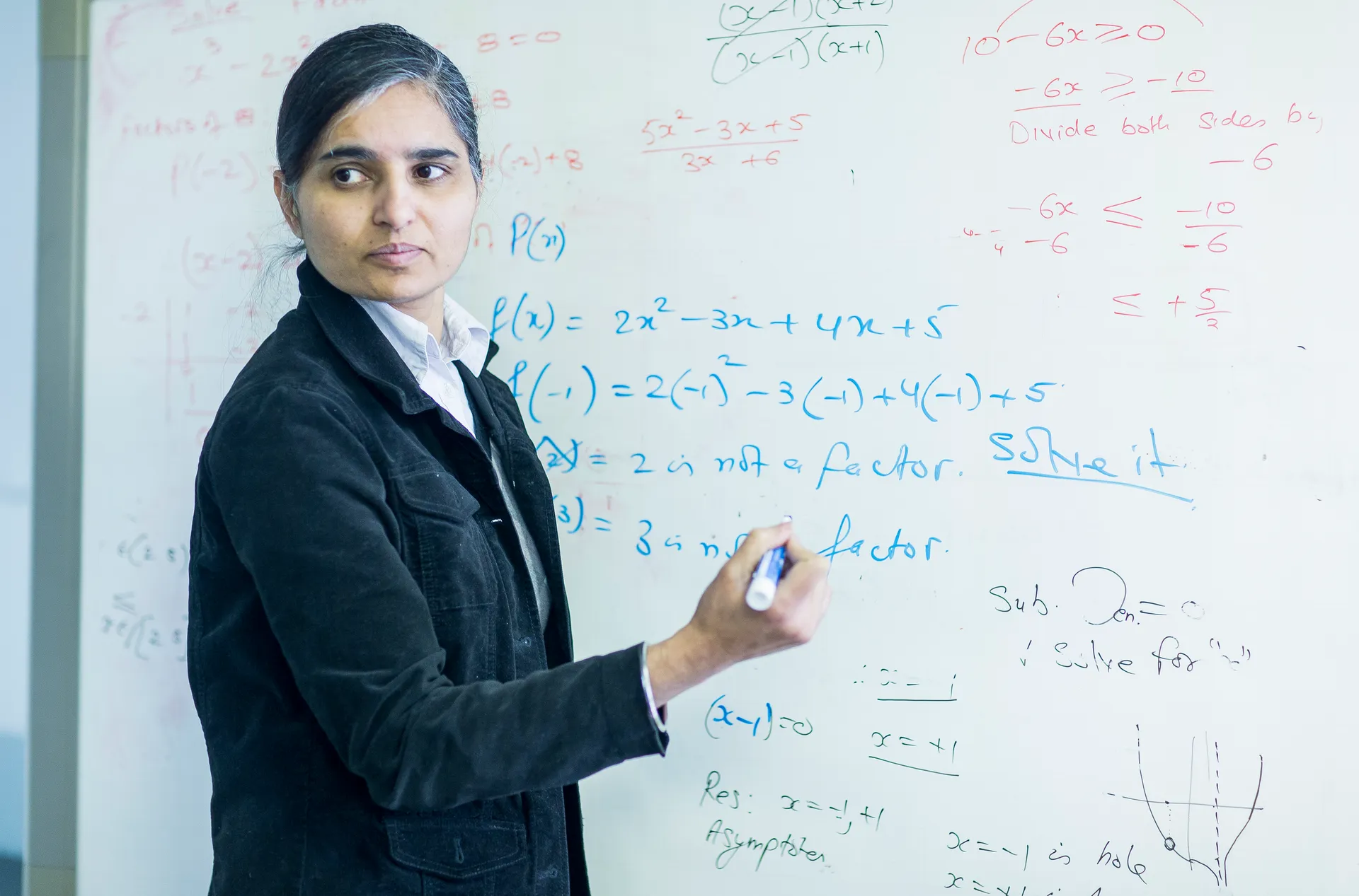 A Vaughan College math teacher writes equations on a whiteboard, glancing back at the class