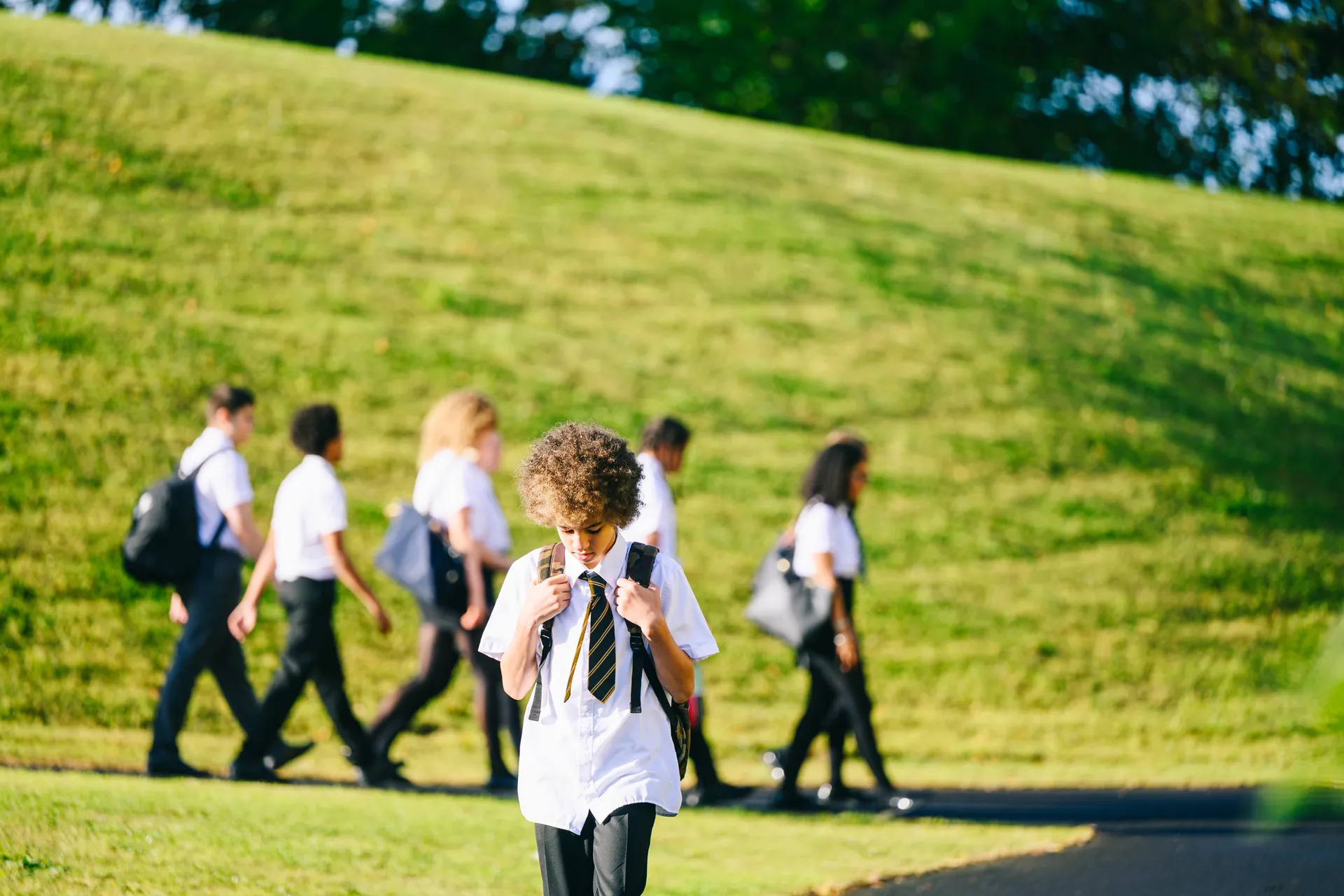 A Vaughan College student walking to school along a tree-lined path, classmates in the background