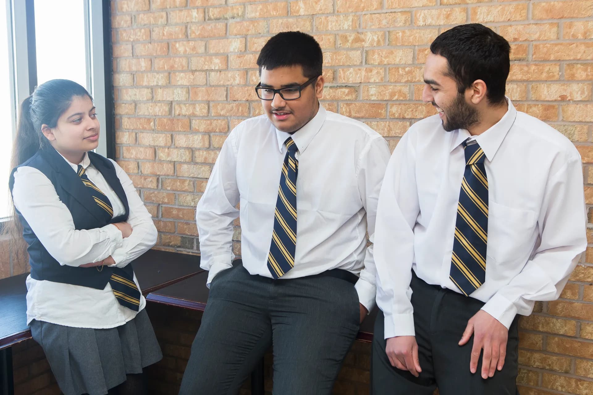 Three Vaughan College students in uniform talking together against a sunlit brick wall between classes
