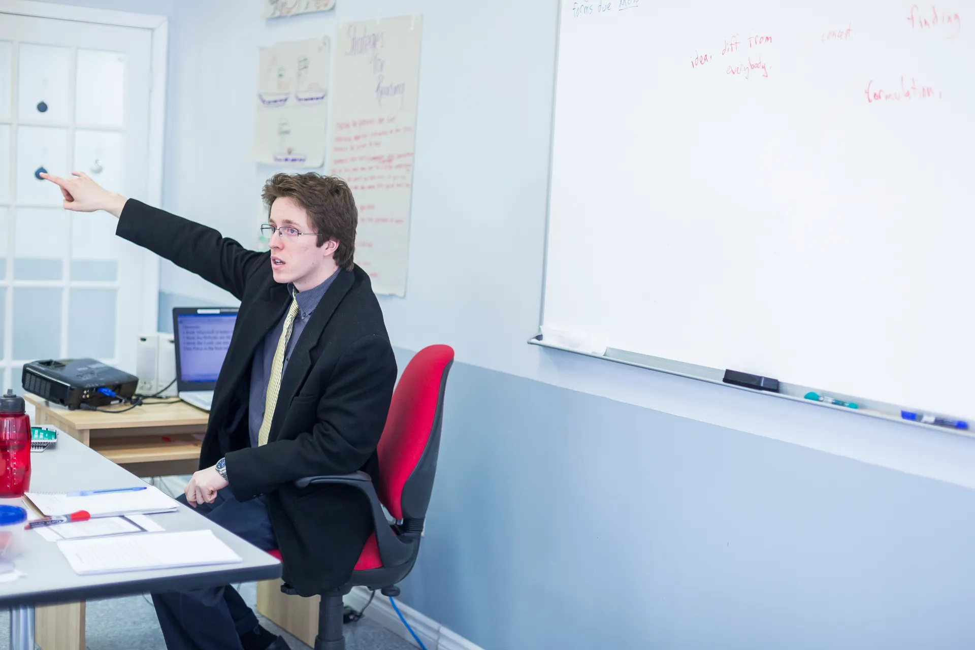 A Vaughan College teacher gestures while leading a senior class, whiteboard with student notes behind him