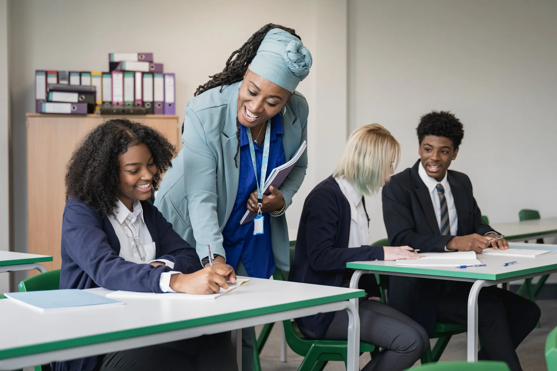 A Vaughan College teacher leaning over a desk to help students in uniform with their work