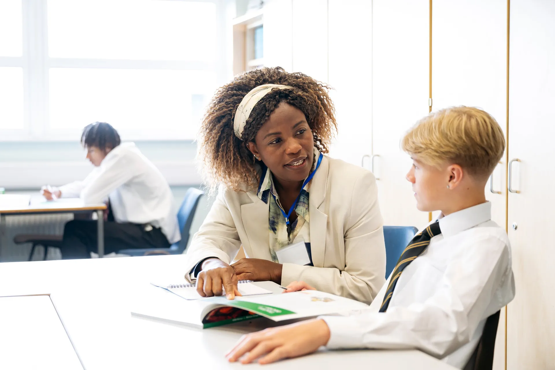 A Vaughan College teacher working through a textbook one-on-one with a student in uniform