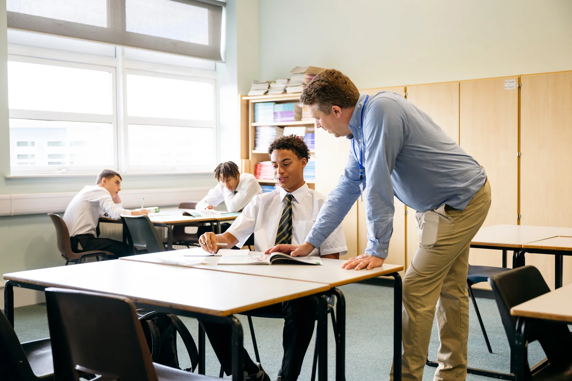 A Vaughan College teacher leaning in to support a student with classwork at a desk