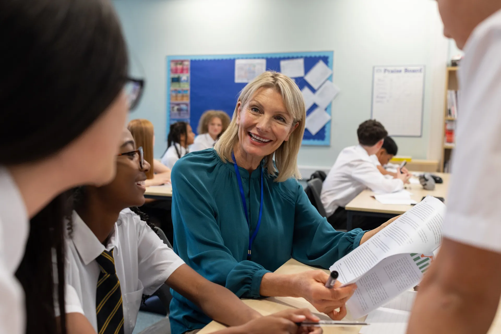 A Vaughan College teacher in conversation with two students in uniform beside a sunlit classroom window