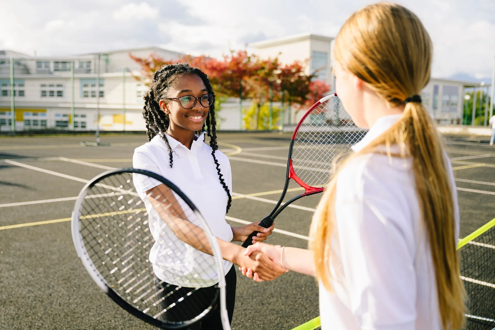 Two Vaughan College students shaking hands with tennis racquets after a match