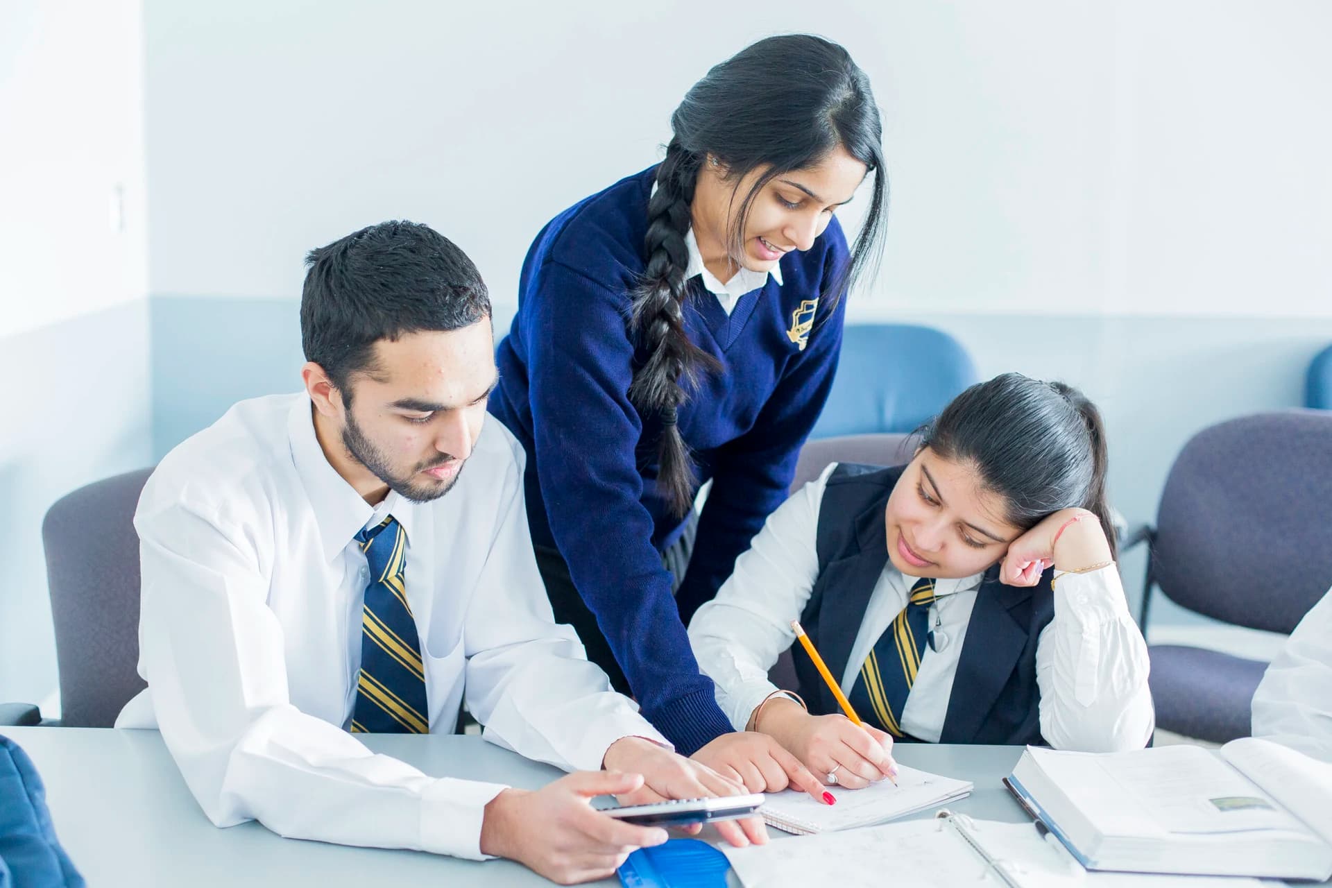 Three Vaughan College students in navy uniform working through a problem together at a desk, one leaning in to help